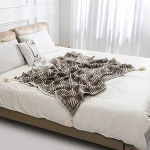 Close-up of a Bohemian knitted throw blanket with tassels spread on a white bed.