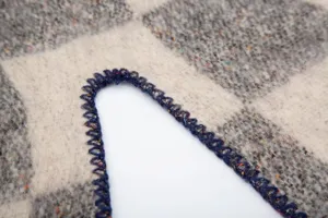 Gros plan du châle à carreaux en mohair avec finition de bord au point de feston bleu.