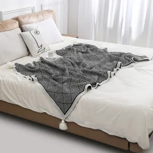 Bohemian knitted throw blanket with geometric diamond pattern and white tassels on a bed