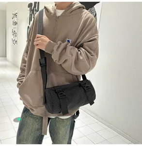 Urban lifestyle shot of a black checkered cylinder crossbody bag worn by a male model