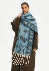 Ethnic style blue jacquard scarf with tassels worn by model over a brown winter wool coat.