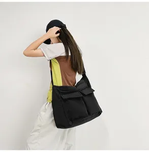 Detailed side view of a large black canvas messenger bag shown on a female model