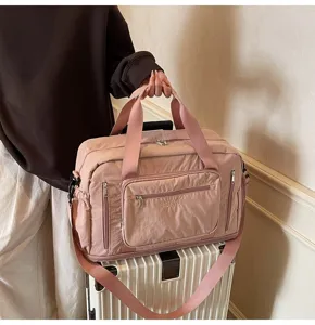 Pink large capacity travel duffle bag with adjustable strap shown on a white suitcase