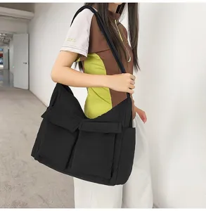 Detail view of a large black canvas messenger bag with pockets worn by a model