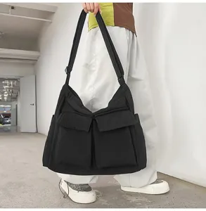 Large black canvas crossbody bag with front pockets worn in a minimalist urban setting.