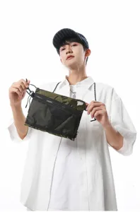 Asian male model holding a green tactical crossbody bag in a Japanese workwear style