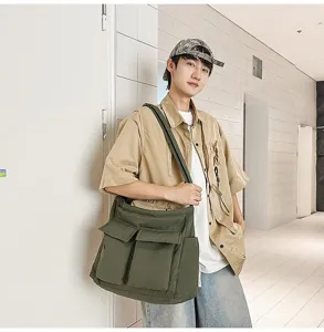 Male model wearing a large olive green canvas crossbody bag in a casual indoor setting.