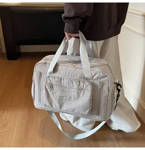 Detailed view of large grey nylon travel bag with shoulder strap and handles in room