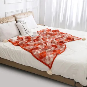 Detail view of bohemian orange checkered knitted throw blanket with tassels on bed.