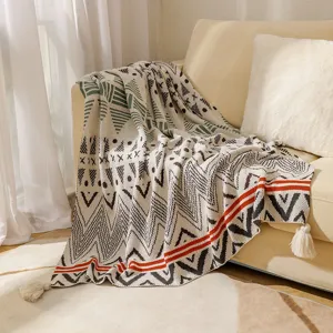Bohemian style knitted throw blanket with tassels and tribal geometric pattern on sofa.