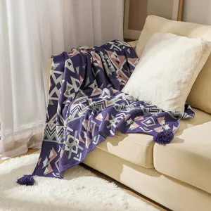 Bohemian knitted throw blanket with geometric patterns and purple tassels on a sofa