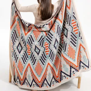 Back view of a person holding a large bohemian knitted blanket with geometric patterns.