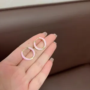 Detailed macro view of elegant pink enamel geometric hoop earrings held in a hand