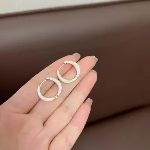 Close-up of elegant white enamel geometric hoop earrings held on fingers for scale