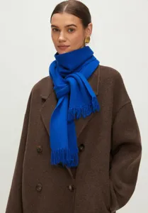 Detailweergave van een felblauwe gebreide sjaal met franjes over een bruine wollen winterjas