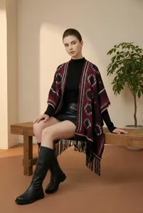 Detailed shot of a woman wearing a bohemian wine red fringe poncho sitting on a bench.