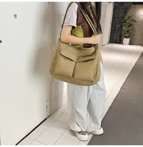 Detail view of large khaki canvas crossbody bag with two front pockets worn by a model