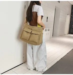 Model wearing a large khaki canvas messenger bag in a minimalist modern indoor hallway