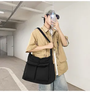 Male model wearing a large black retro canvas messenger bag in a street style setting