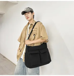 Large black canvas messenger bag for students, shown on model in a minimalist hallway.