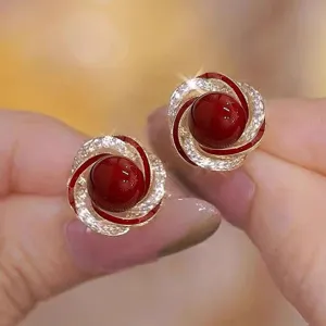 Close-up of elegant gold-toned swirl earrings with red beads and pavé crystals.