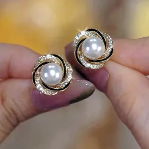 Close-up of elegant pearl stud earrings with sparkling crystals and black enamel swirl design.