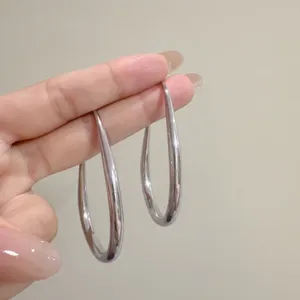 Detailed view of oversized polished silver teardrop hoop earrings held on fingers