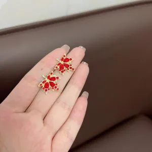 Close-up of gold-tone maple leaf earrings set with vibrant red rhinestones on hand