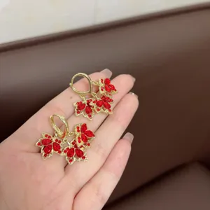 Close-up of gold-plated earrings featuring intricate red crystal maple leaf design