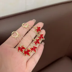 Close-up detail of elegant long gold dangle earrings with red crystal maple leaf charms.