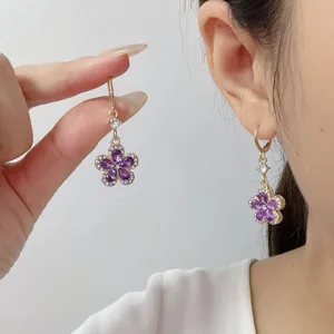 Détail de boucles d'oreilles fleurs violettes avec strass portées par un mannequin