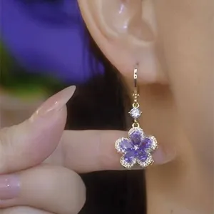 Détail de boucles d'oreilles style coréen avec pétales de fleurs violettes et strass brillants.