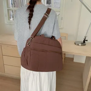 Back view of a large brown quilted travel bag worn over the shoulder in a minimalist room