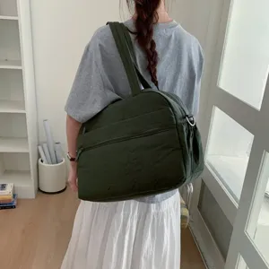Rear view of a large dark green quilted cloud gym bag carried over shoulder by a woman