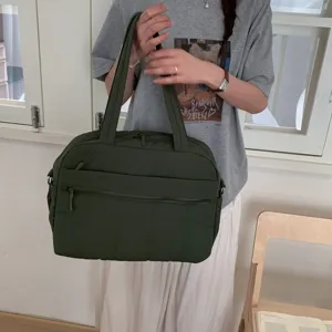 Detailed view of large dark green quilted travel bag held by model in casual setting
