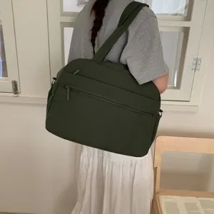 Detail showing a large green cloud travel bag carried by a model in a minimal indoor setting.