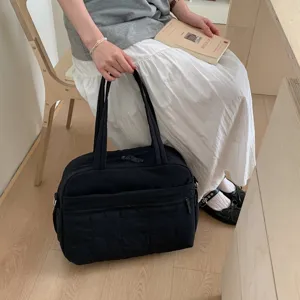 Detail view of a black quilted cloud travel bag held by a model in a minimal setting.