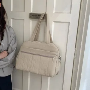 Cream quilted large capacity travel tote bag hanging on a white door