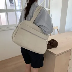Large beige quilted cloud travel bag shown being worn on the shoulder by a model in a room