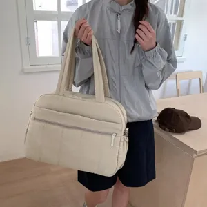 Close-up detail of a large cream quilted cloud travel bag being held by a lifestyle model