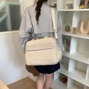 Back view of a woman carrying a large beige quilted cloud travel bag in a modern room