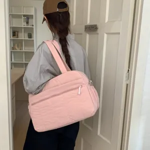 Lifestyle detail showing a large pink quilted cloud travel bag being carried on the shoulder