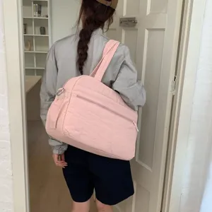 Large pink quilted travel duffel bag for women worn over the shoulder by a fashion model