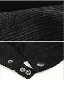 Close-up detail of black corduroy fabric and metal snap buttons on a beret hat.