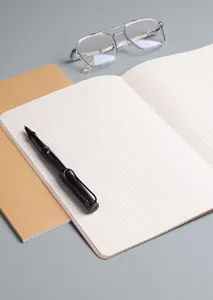 Detailansicht eines offenen Gitter-Notizbuchs mit Kraftpapier-Einband auf grauem Tisch.