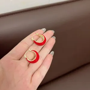 Close-up of red enamel U-shaped hoop earrings with gold-tone finish on hand.