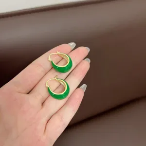 Close-up detail view of retro U-shaped green hoop earrings with gold finish shown on hand