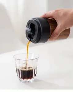 Action shot of coffee pouring from a stylish wood grain travel mug into a glass cup