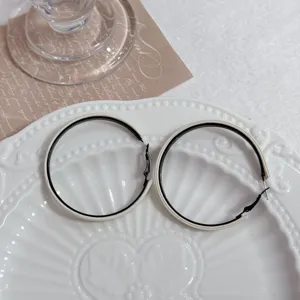 Close-up of large black and beige geometric hoop earrings on a white ceramic plate.