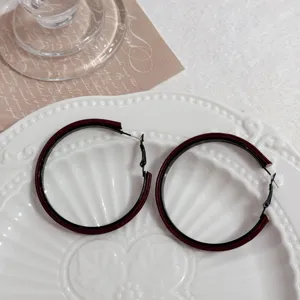 Detailed view of large burgundy and black geometric hoop earrings on a plate